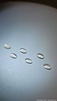 Six translucent oval white moonstones, cabochon cut, displayed on white background under light showing adularescence.