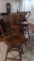 Three solid oak swivel bar stools with etched pattern on backrests arranged near a dining table.