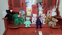 Wide view of a collection of 12 Beanie Babies including specialty and McDonald's editions arranged on wooden furniture. Bears vary in colors and patterns, some in original packaging, all with visible Ty heart tags.