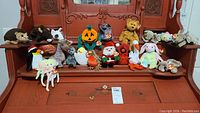Front view of 20 Beanie Babies displayed on wooden furniture showing a variety of different animal characters including a pumpkin and holiday themed ones.