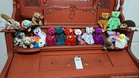 Overview of 20 assorted Beanie Babies plush toys displayed on a wooden bench with various colors and animal designs; visible TY heart tags attached to each plush.