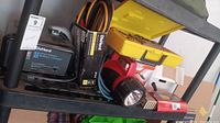 Overview of the DieHard battery charger, jumper cables, flashlight, road assistance kit, and sanding disc on a black shelf.