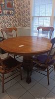 Round oak dining table with four matching chairs shown in a dining room setting, highlighting the table's round top and pedestal base.