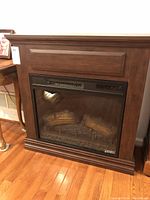 Front view of the electric fireplace with wooden mantel and faux logs visible inside glass panel.