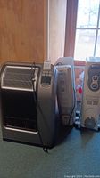 Three heaters lined up: Lasko heater with digital controls and ceramic element front left, white DeLonghi heater behind missing a wheel, and white Pelonis heater on far right.