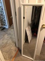 Full length white frame mirror leaning against wall near door