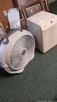 Photo showing white Kenmore humidifier and WindMachine white fan on carpeted floor, items need cleaning.