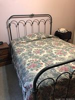 Full view of queen size iron bed with floral quilt set and headboard.