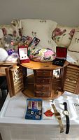 Photo of wooden oval jewelry box with drawers open, multiple jewelry boxes on top, men's and women's jewelry items including watches, cuff links, sunglass case, and perfume sample.