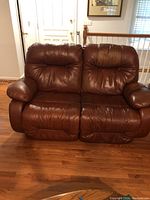 Front view of brown leather loveseat showing two seats with plush cushions and armrests.