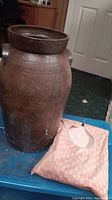 Tall brown pottery jar and pink clothespin bag with small floral print and zipper opening, placed on blue table.