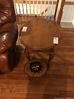 Oval oak Queen Ann style side table with oval top, one drawer with brass handle, and carved legs. Tree stump stool with raccoon face decal beneath the table.