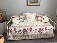 Front view of white metal trundle day bed with floral pink bedding and pillows arranged neatly on the bed.