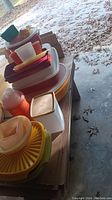 Various vintage Tupperware plastic containers and bowls in several colors stacked on cardboard.