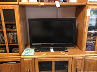 Vizio TV placed inside a wooden cabinet with remote control and cables on shelf below TV.