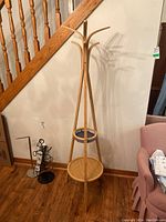 Full view of the coat rack near a stair railing, showing the overall height and design including hooks and the circular table base.