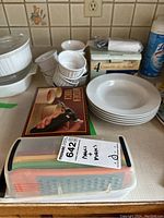 Photo showing creme brulee torch box, stacked white ramekins and bowls, colorful grater set in transparent case, and boxed Hudson Bay bowls.