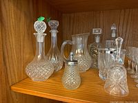 Overall view of the 8-piece lot showing 4 decanters with stoppers, crystal ice bucket, glass pitcher, crystal bell, and oil decanter with metal spout.