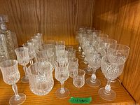Wide angle showing full set of crystal stemware and glassware on wooden shelf with various sizes in rows