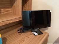 Full front and angled view of the Dell monitor showing screen, base, and power cable, placed on a wooden shelf.