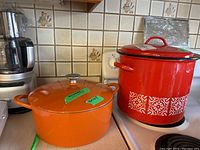 Orange Mario Bateli Dutch oven beside red enamel canning pot on kitchen counter, showing both items together.