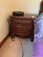 Wood end table with two drawers, polished medium brown wood, ornate metal handles, showing scratches and some wear on the surface.