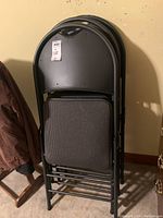 Four black metal and cloth folding chairs stacked together showing the seat and backrest design and folding mechanism.