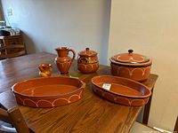 Full lot of 6 terracotta glazed pottery pieces on wood table showing pitchers, lidded jars, and serving dishes