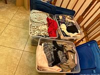 Three lidded clear plastic bins filled with assorted ladies clothing, showing variety of colors and patterns.