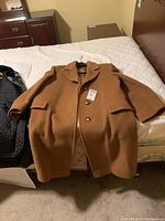 Camel/tan wool coat laid flat on bed showing front front buttons, flap pockets, and notched collar