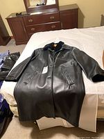 Full length black leather coat displayed laid out on bed, showing front and length.