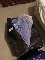 Large black bag with multiple men's shirts visible inside, various checkered patterns in blue, red and white hues.