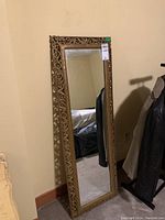 Full view of the framed mirror leaning against a wall, showing its height and decorative frame.