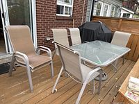 Full set showing the rectangular glass top table, six matching chairs with poly fabric upholstery, and cast metal umbrella stand on an outdoor wooden deck.