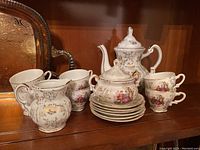 Front view of the entire tea service set including the teapot, creamer, sugar bowl, cups and saucers arranged on a wooden surface with a decorative backing.