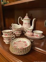Full display of pink bone china tea set including cups, saucers, teapot, sugar bowl, creamer
