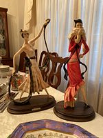 Pair of two figurines on wooden bases, one in red dress and one in cream pleated dress