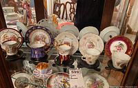 Display of six teacups and six saucers with various designs and colors on glass shelf