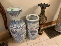 Photo showing all three tall vases grouped together, two ceramic with painted details, one metal with gold motifs and scalloped top.