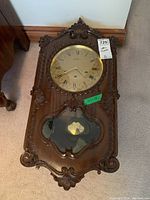 Front view of wooden Reguladora wall clock showing clock face, ornate wood carvings, and pendulum compartment with visible pendulum.