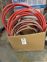 Photo of three coiled hoses in a cardboard box, two red air hoses and one red heavy duty water hose, showing worn condition.