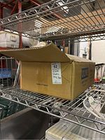 Box labeled with ULINE brand containing plastic bags, placed on a metal shelf in a storage or warehouse setting.