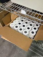 Box of white thermal paper rolls for business receipt printers, unopened and tightly packed.