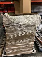 Large skid of new, flattened cardboard boxes wrapped in plastic, stored in warehouse.