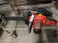 Full view of the electric chainsaw showing the red body, black blade cover and black fabric dust cover with Homelite branding.