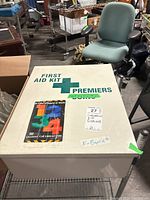 Closed large metal first aid box with 'Premiers' branding and first aid cross symbol on lid; sticker indicating industrial first aid kit.