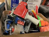 Box filled with red-and-gray tape dispensers, paint brushes, and various clamps
