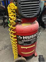 Front view of red vertical Husky air compressor with yellow coiled hose and wheels