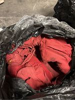 Large black bag containing red cotton rags, some rags rolled or folded, from worn cotton fabric.