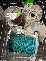 View of six metal wire spools with wires in teal, pink, yellow, and other colors inside a wire cart.